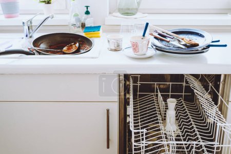 Photo for Pile of dirty unwashed dishes on kitchen surface, small dishwasher, white kitchen facades. Dirty dishes in kitchen. Small Kitchen with integrated dishwasher, white fronts - Royalty Free Image