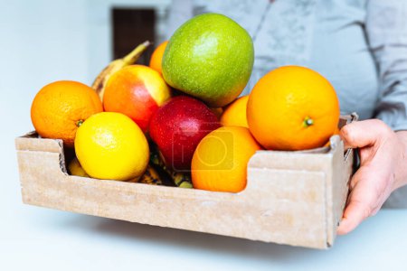 Foto de Caja de cartón con frutas, manzanas y naranjas, en manos mujer - Imagen libre de derechos