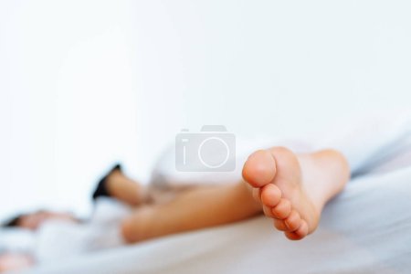 Téléchargez les photos : Adolescente dormant, pieds nus regardant sous la couverture, suspendue au lit. Concept de sommeil sain - en image libre de droit