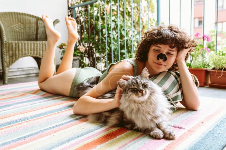 Téléchargez les photos : Curly jeune fille attrayante fait du yoga, relaxant, assis sur le balcon en haut vert, avec chat bien-aimé. Loisirs avec concept chat - en image libre de droit