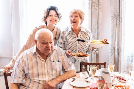 Foto de La abuela positiva familiar la nieta abuelo, juntos, con la sonrisa, poniendo la mesa, la preparación para la cena de fiesta. Familia judía sirve alegremente mesa de fiesta - Imagen libre de derechos