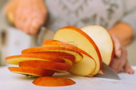 Téléchargez les photos : Womans main utilise un couteau de cuisine pour couper de grosses pommes mûres en tranches, pour faire davantage de croustilles de pomme, pour cuire la tarte. - en image libre de droit