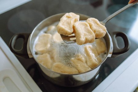 woman cooks lazy dumplings in boiling water, on an electric hob, takes out ready-made hot lazy dumplings from pan