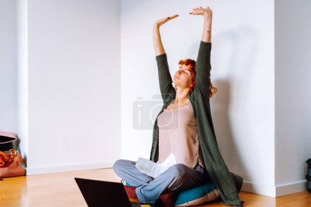 Porträt rothaarige Teenagerin, die auf dem Boden in einem leeren, unmöblierten Zimmer sitzt, Tablet benutzt, unmontierte Koffer in der Nähe stehen, Konzept umzieht, Wohnraum für Studenten anmietet, zu Hause online studiert