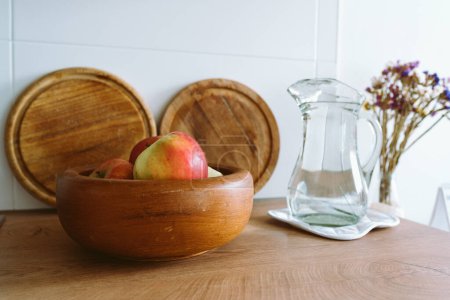 schöne Küche Hintergrund in hellen Farben, mit einem Holzteller mit Obst, Strauß Blumen, Glaskrug Wasser. Im Vordergrund. Öko-Gerichte, Küche in einer Wohnung mit modernem Interieur