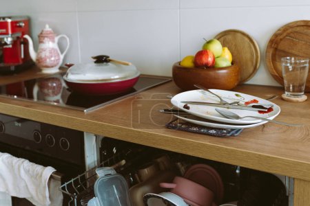 vaisselle sale usagée sur comptoir de cuisine en bois, avec lave-vaisselle intégré. mobilier moderne, concept de nettoyage de cuisine