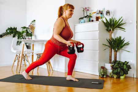 mujer de mediana edad, rubia, con curvas, hace yoga en habitación amplia y luminosa con plantas de la casa, en el interior del hogar, positividad corporal