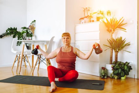 mujer de mediana edad, rubia, con curvas, hace yoga en habitación amplia y luminosa con plantas de la casa, en el interior del hogar, positividad corporal