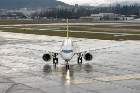 Foto de Zurich, Suiza, 17 de enero de 2024 YL-AAR Air Baltic Bombardier CS-300 o Airbus A220-300 viajan en taxi a lo largo del delantal durante una ducha de lluvia - Imagen libre de derechos