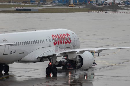 Foto de Zurich, Suiza, 17 de enero de 2024 HB-JBF Aviones suizos Airbus A220-100 o Bombardier CS-100 son remolcados a lo largo del delantal durante una ducha de lluvia - Imagen libre de derechos