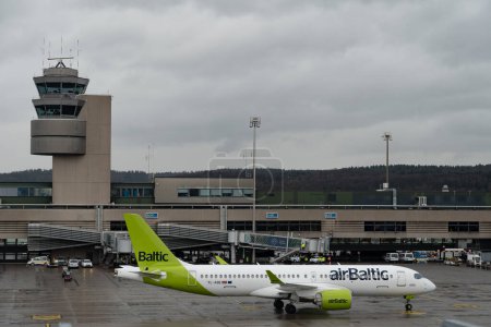 Foto de Zurich, Suiza, 18 de enero de 2024 YL-ABE Air Baltic Bombardier CS-300 o Airbus A220-300 viajan en taxi a la puerta durante una ducha de lluvia - Imagen libre de derechos