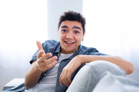Photo for Hispanic teenager boy sitting on couch talking and looking to camera - Royalty Free Image