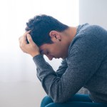 Sad hispanic teenager boy sitting hands on head. Depression, anxiety, stress and mental health concept