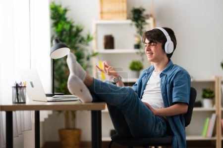 Téléchargez les photos : Teenager having video conference. Relaxing boy talking on laptop with feet on desk at home. - en image libre de droit