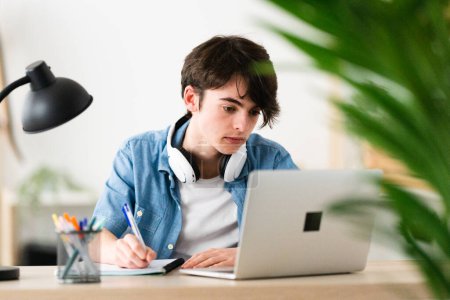 Téléchargez les photos : Teenager boy watching tutorial on laptop. Student learning  online - en image libre de droit