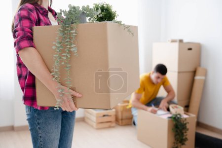 Téléchargez les photos : Femme méconnaissable tenant une boîte en carton. Jeune couple déménageant à domicile. - en image libre de droit