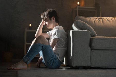 Besorgter Teenager, der nachts auf dem Boden sitzt. Person überdenkt im Wohnzimmer