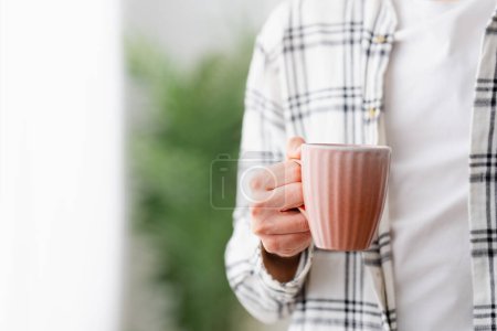 Gros plan d'un jeune homme méconnaissable tenant une tasse de café à la maison
