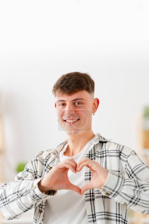 Vertikales Foto eines glücklichen Mannes, der zu Hause mit Händen Liebe gestikuliert