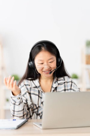 Téléchargez les photos : Photo verticale d'une femme chinoise faisant un geste lors d'une réunion en ligne avec un casque et un ordinateur portable - en image libre de droit