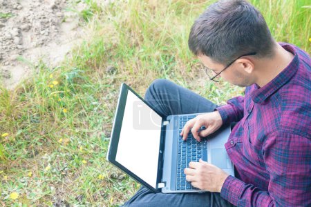 Foto de Un joven trabaja en un portátil al aire libre. Hombre trabajando en la computadora. Trabajo al aire libre - Imagen libre de derechos