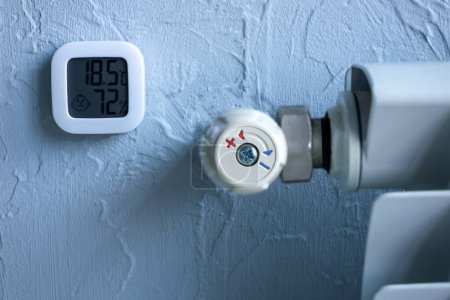 Radiador de calefacción con regulador de temperatura. Un termómetro que muestra grados y humedad en el apartamento. Calefacción de gas de invierno.