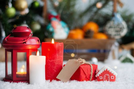 Téléchargez les photos : Bougies de Noël et cadeau avec des étiquettes pour écrire. En arrière-plan se trouve un arbre de Noël et des cadeaux avec des lumières. Nouvel an fond. - en image libre de droit