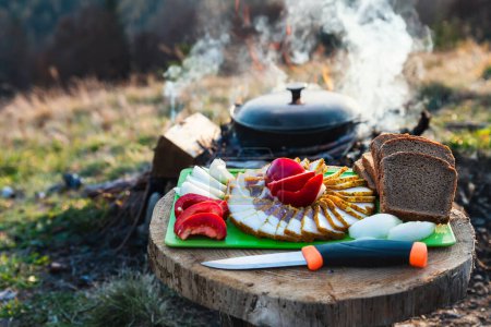 Téléchargez les photos : La nourriture est préparée dans un chaudron au camping. Graisse et pain noir aux légumes sur une table en bois. - en image libre de droit