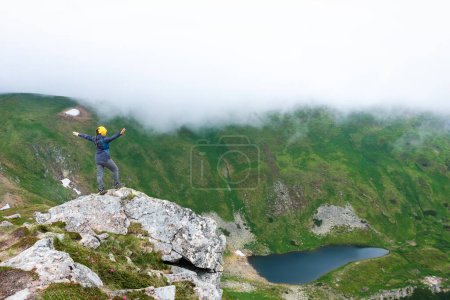 Photo for The girl is standing on a rock above the lake. View of mountain lake Brebeneskul. The highest mountain lake in Ukraine. Top view. - Royalty Free Image