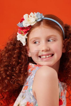 Smiling Redhead Girl with Freckles in Blue Floral Dress on Orange Background