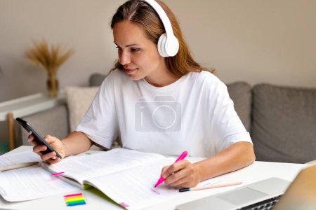 Foto de Una estudiante universitaria está viendo un video educativo en Internet usando su teléfono inteligente y auriculares. - Imagen libre de derechos