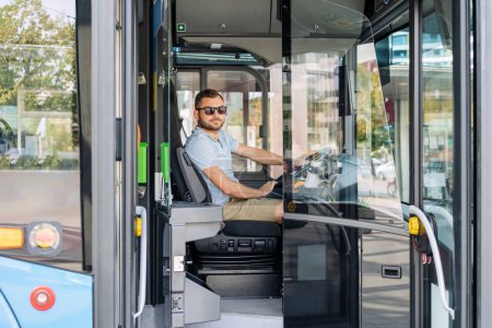 Foto de Joven hombre adulto conductor de autobús de la ciudad se sienta en la cabina del conductor mientras espera a los pasajeros en la parada de autobús. - Imagen libre de derechos