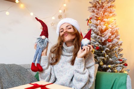 Photo for Childishness during Christmas holidays. Woman wearing Santa hat has fun with xmas presents. - Royalty Free Image