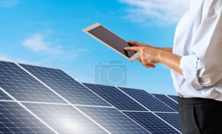 Una mujer vestida con ropa formal controla la estación de energía solar de forma remota usando una tableta digital.