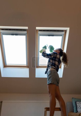 Téléchargez les photos : Femme nettoie fenêtre puits de lumière dans son appartement. Travaux ménagers, nettoyage des fenêtres de toit à la maison. - en image libre de droit