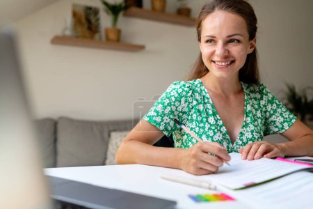 Téléchargez les photos : Apprentissage en ligne pour adultes. Jolie femme brune souriante tout en utilisant le classeur à la maison. Élégance éducative. - en image libre de droit
