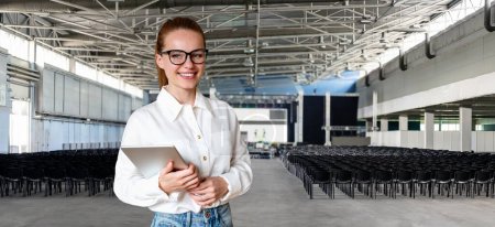 Businesswoman and conference hall with empty chairs and blurred stage.