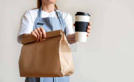 Takeaway food concept. Waitress giving coffee cup and paper bag with meal to customer.