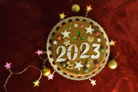 Gâteau du Nouvel An pour 2023, lumières de Noël en forme d'étoile et boules sur nappe en velours rouge