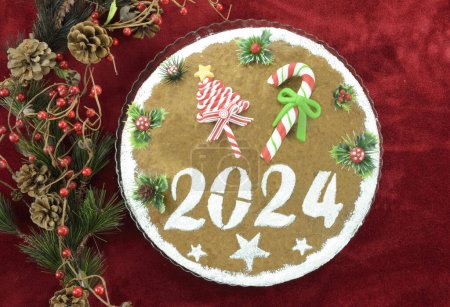 2024 Neujahrskuchen und künstliche Weihnachtsdekoration auf rotem Hintergrund