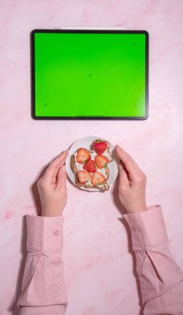 Téléchargez les photos : Femme tenant fromage à pâte molle et sandwich à la fraise près de la tablette écran vert, concept d'alimentation saine et l'alimentation, en utilisant l'application de comptage des calories, vue du dessus, photo de haute qualité - en image libre de droit