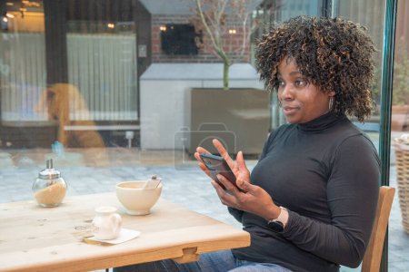 Foto de African american woman without makeup talking on smartphone in cafe in the morning,The concept of rest from household chores, the woman took the child to school and is resting, High quality photo - Imagen libre de derechos