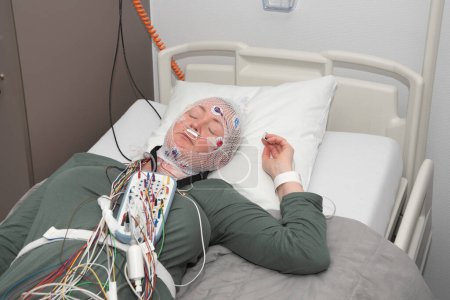 Téléchargez les photos : Femme d'âge moyen mesurant les ondes cérébrales, examinant la polysomnographie en laboratoire du sommeil, photo de haute qualité - en image libre de droit