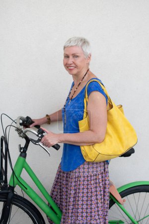 Téléchargez les photos : Joyeux style habillé femme cycliste loue un vélo électrique public, femme en âge actif menant un mode de vie sain, photo de haute qualité - en image libre de droit