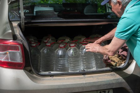 male volunteer loads many five-liter bottles of clean drinking water into the trunk to help victims of a natural disaster. High quality photo