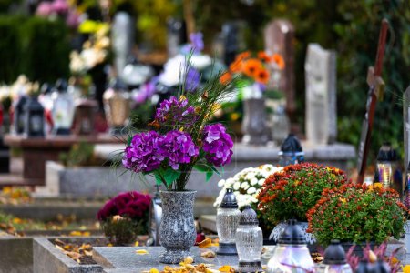 Velas y flores sobre tumbas en el cementerio durante el Día de Todos los Santos. Tomado durante el día, luz natual.