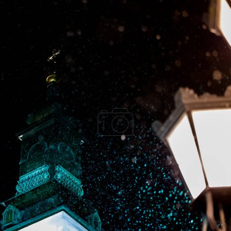 Téléchargez les photos : Illuminated catholic church tower in the evening during a heavy snowfall. Blurred snowflakes in the foreground. - en image libre de droit