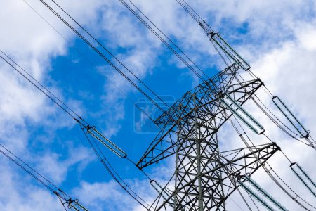 High-voltage pylon against a blue sky with a slight cloud cover. High voltage transmission lines silhouette