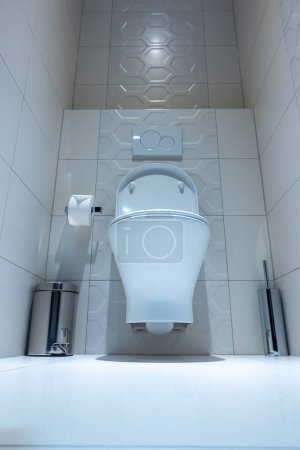 Photo for View of the white toilet bowl in the toilet. Bathroom finished with white glaze tiles and white terracotta. Trash can and brush in the background - Royalty Free Image