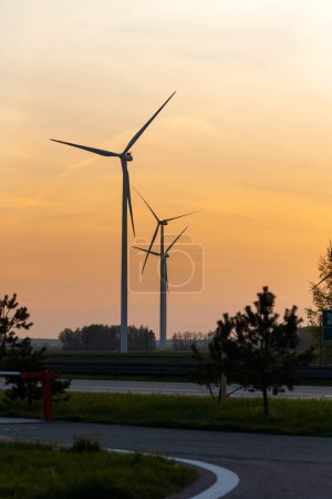 Foto de Turbinas eólicas sobre el fondo de un sol naranja poniente. Fuentes de energía renovables en la lucha contra los elevados costes energéticos - Imagen libre de derechos